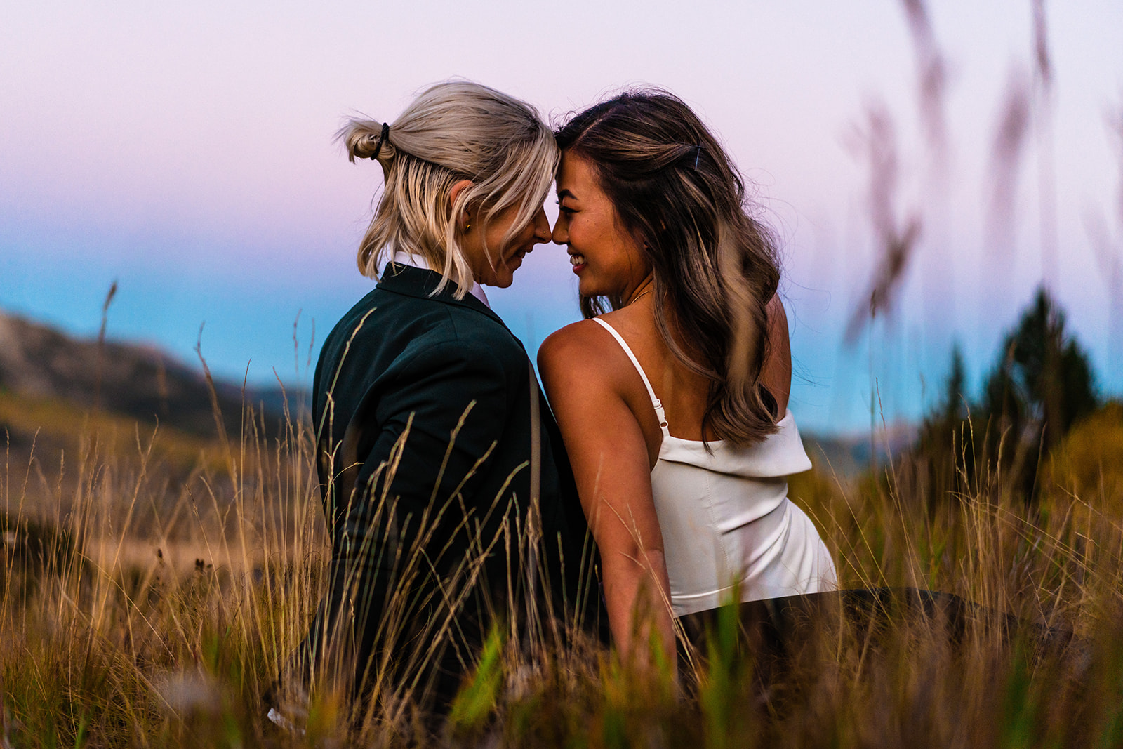 two brides sit together in the grass during their adventure elopement