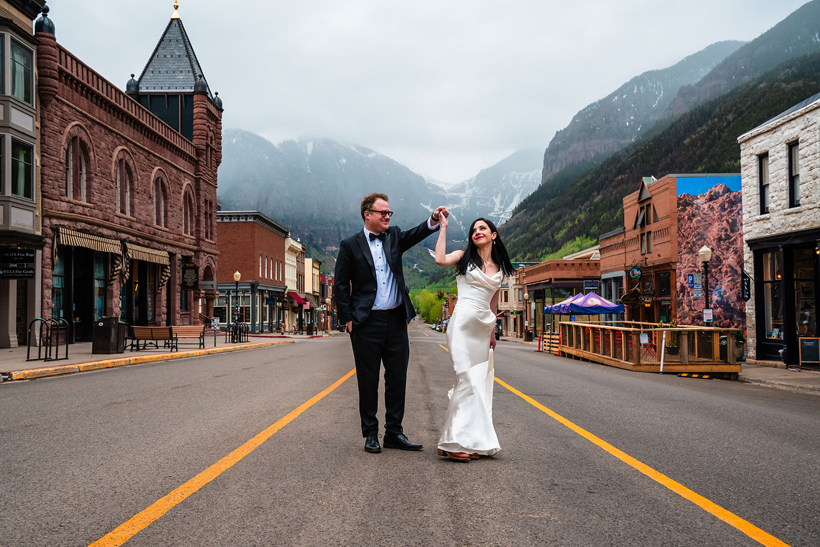 A bride and groom standing in the middle of a street with Telluride mountains in the background during their elopement.
