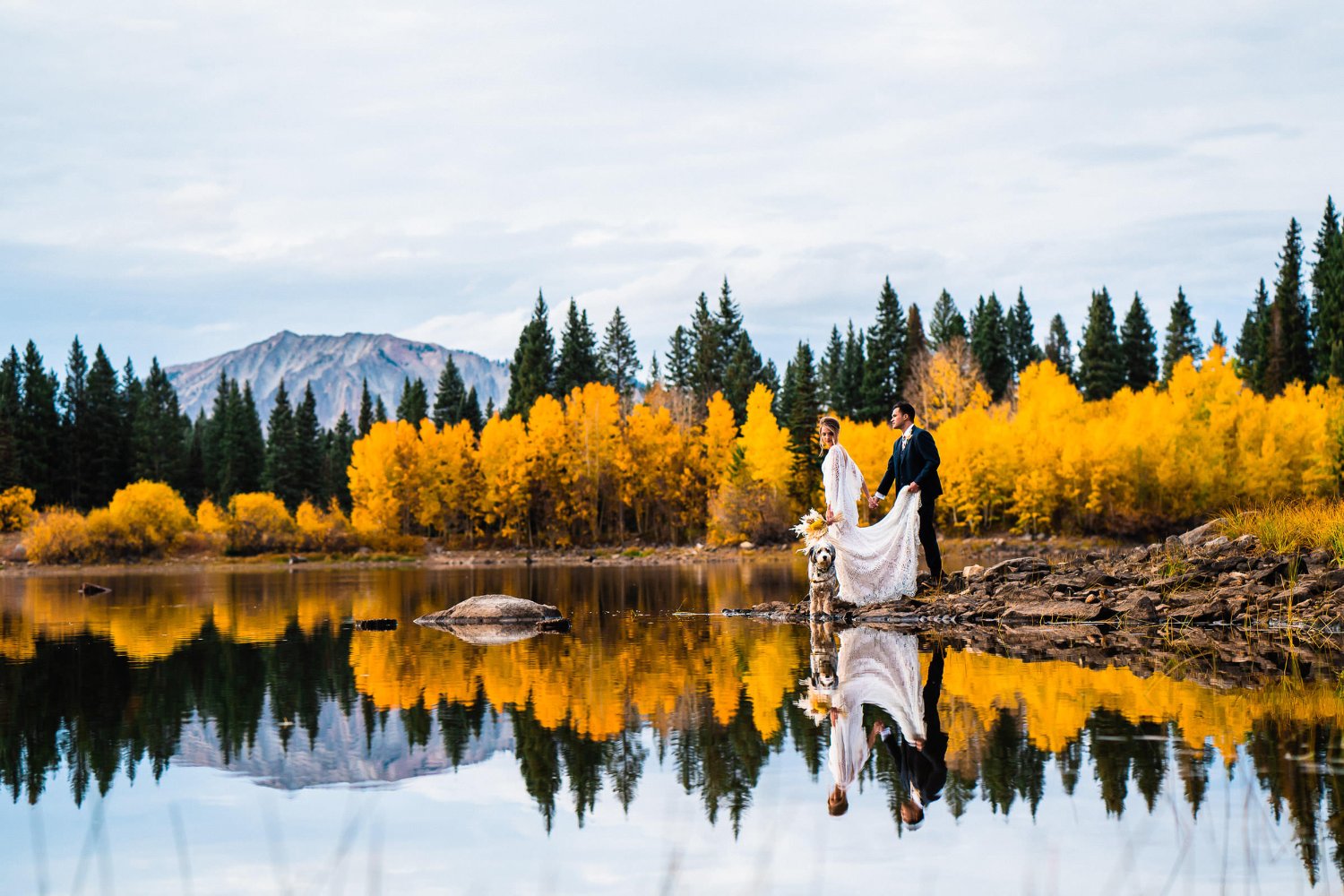 Capturing romantic elopement photos of a beautiful bride and groom amidst the breathtaking autumn backdrop of a serene lake.