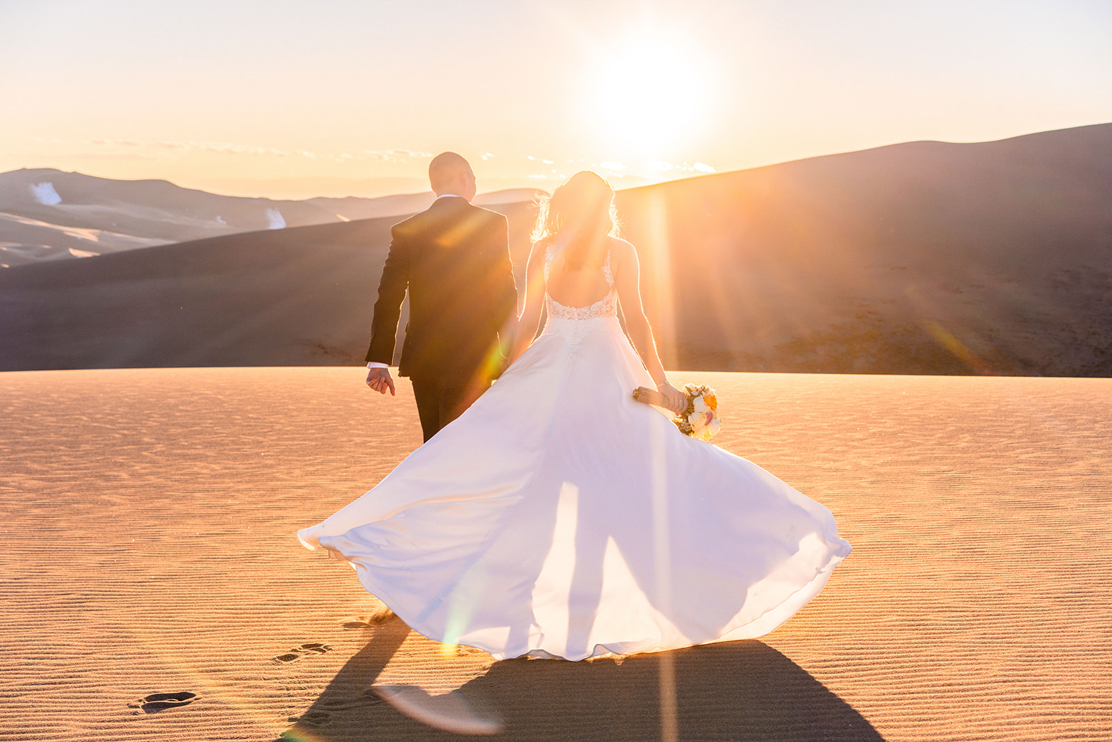 A bride and groom walking through the sand dunes at sunset during their Great Sand Dunes elopement