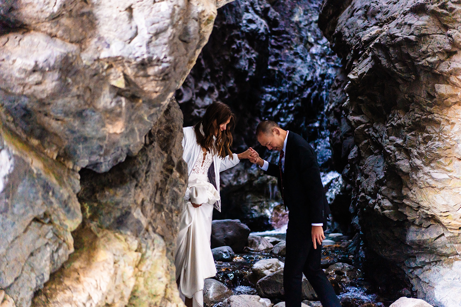 A bride and groom standing next to a stream in a canyon.