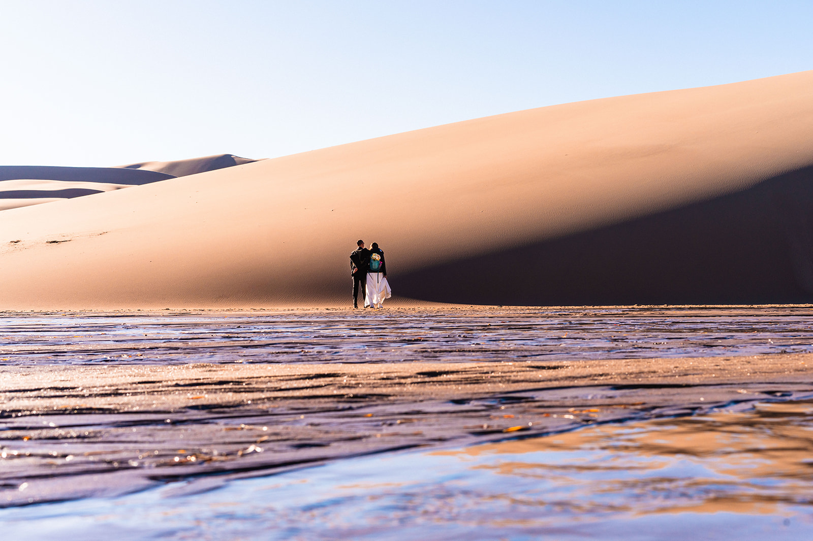 A bride and groom standing in front of a sand dune.