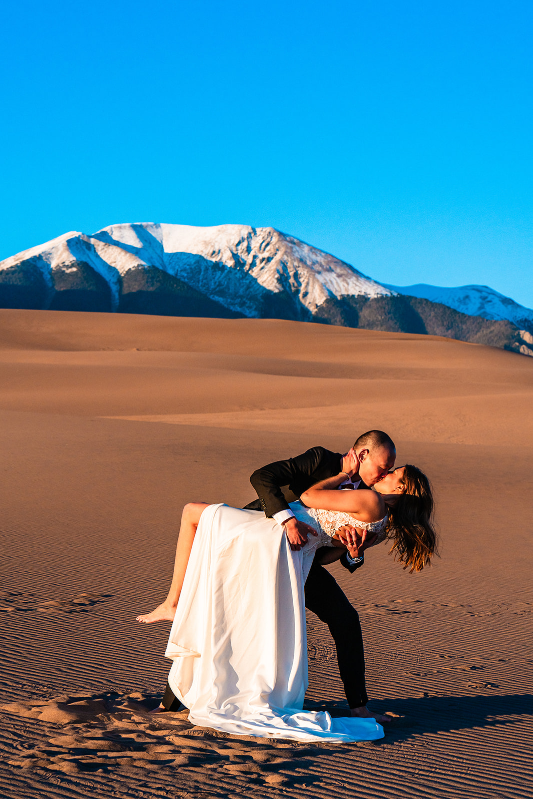 A man and woman kissing in the desert at the Great Sand Dunes