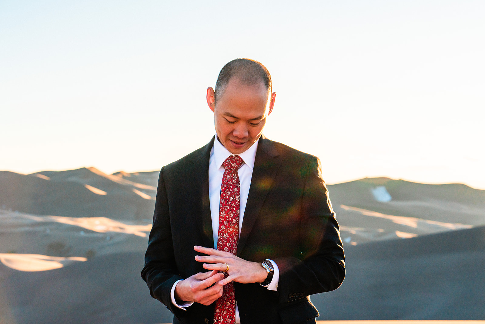 A groom in a suit checking his watch in the desert.