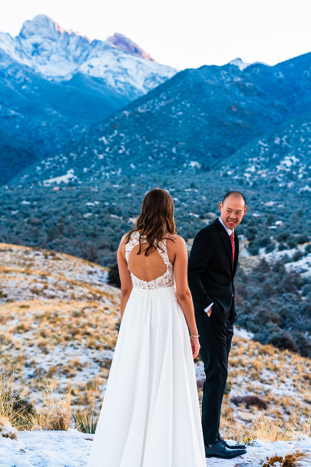 A bride and groom standing in front of a snow covered mountain.