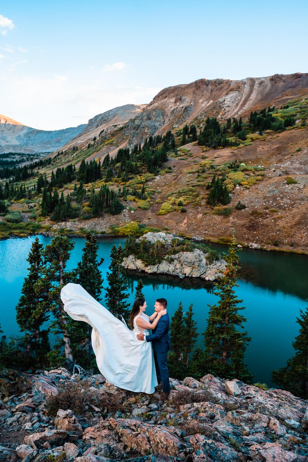 Capture breathtaking elopement photos of a beaming bride and groom on top of a mountain, with stunning views of a serene lake below.