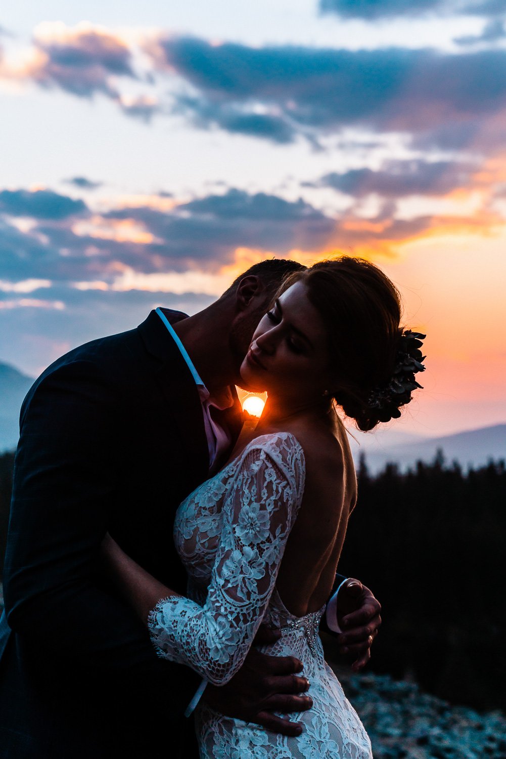 An intimate elopement photoshoot captures a bride and groom embracing at sunset in the mountains.