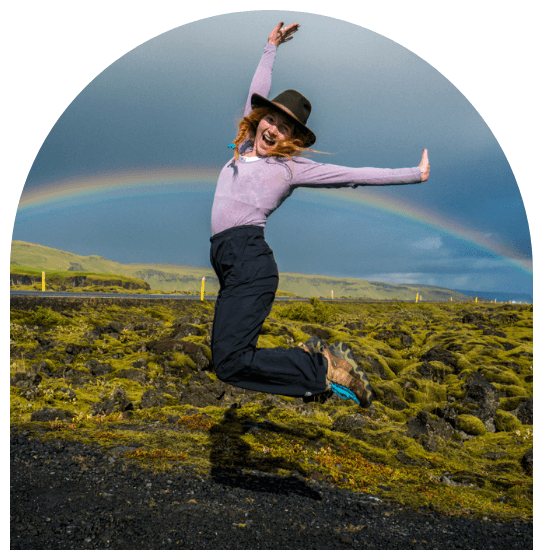 Meg in Iceland jumping in the air with a rainbow in the background