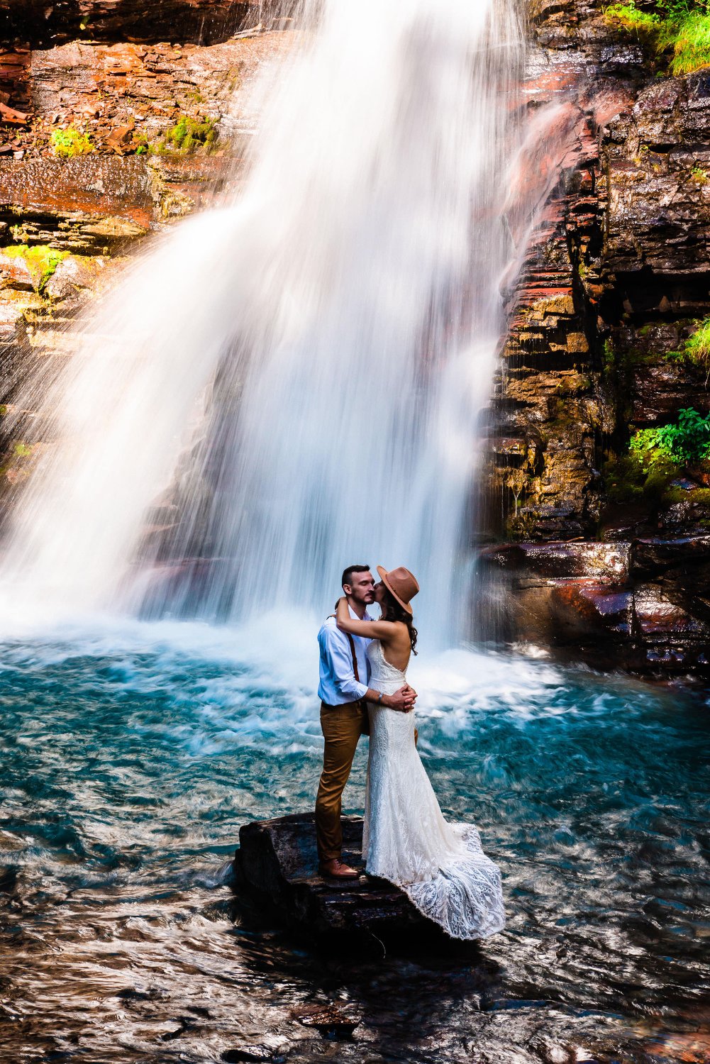 A couple of newlyweds posing for elopement photos in front of a breathtaking waterfall.