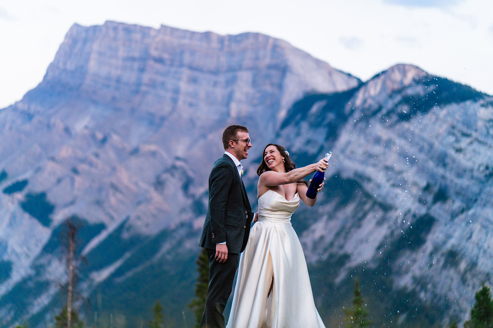 a bride and groom pop champagne with the Colorado mountains behind them