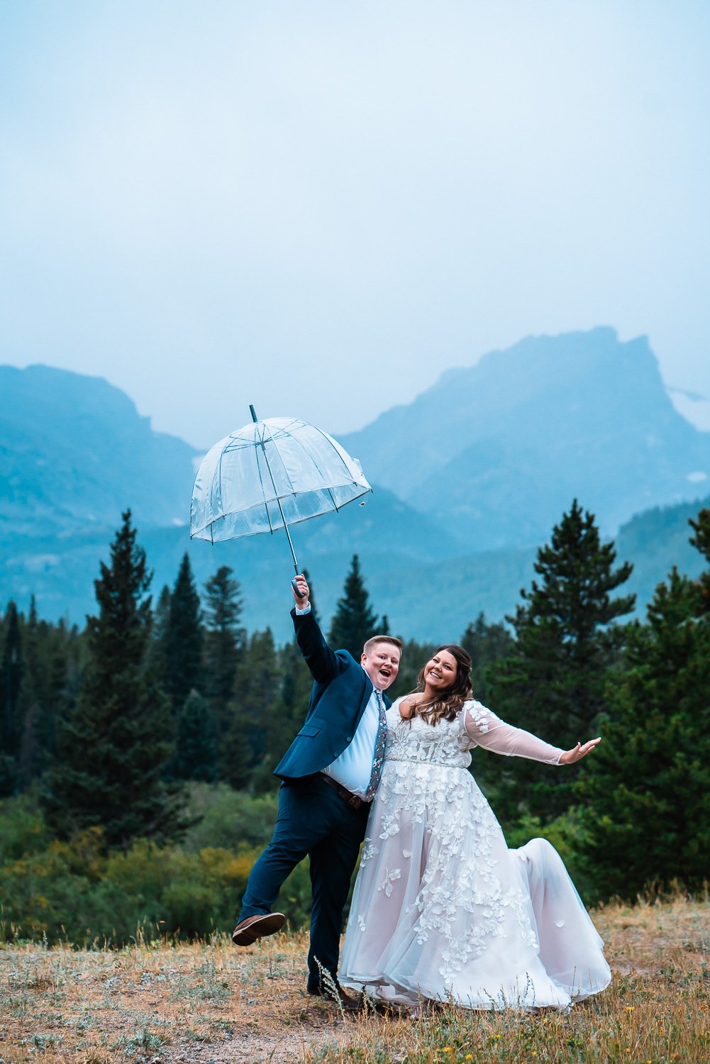 An enchanting elopement photoshoot of a bride and groom holding an umbrella in a beautiful field.