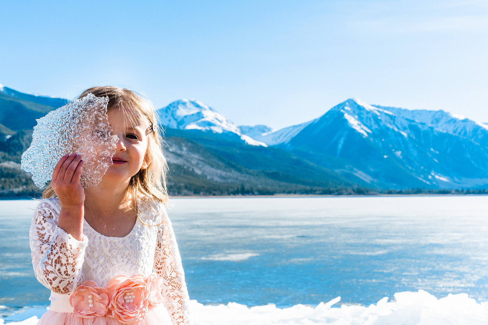 A young girl holds an ice cube in front of the majestic mountains captured by a Twin Lakes Elopement Photographer.