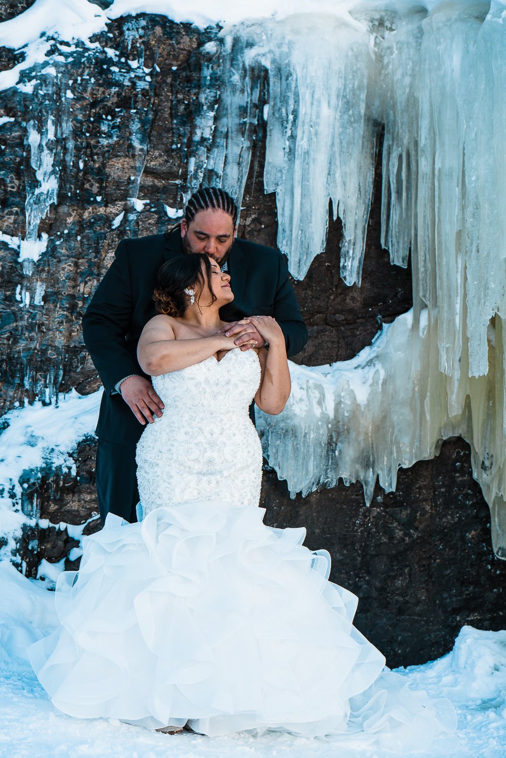 A couple in wedding attire standing before a majestic backdrop of towering icicles, capturing breathtaking elopement photos.