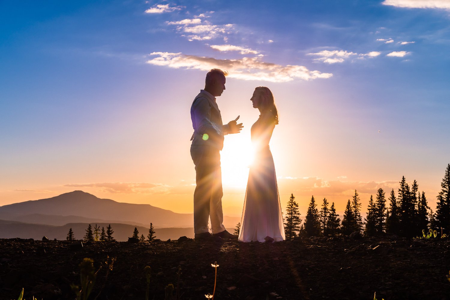 Elopement photos capturing a bride and groom standing on top of a mountain at sunset.