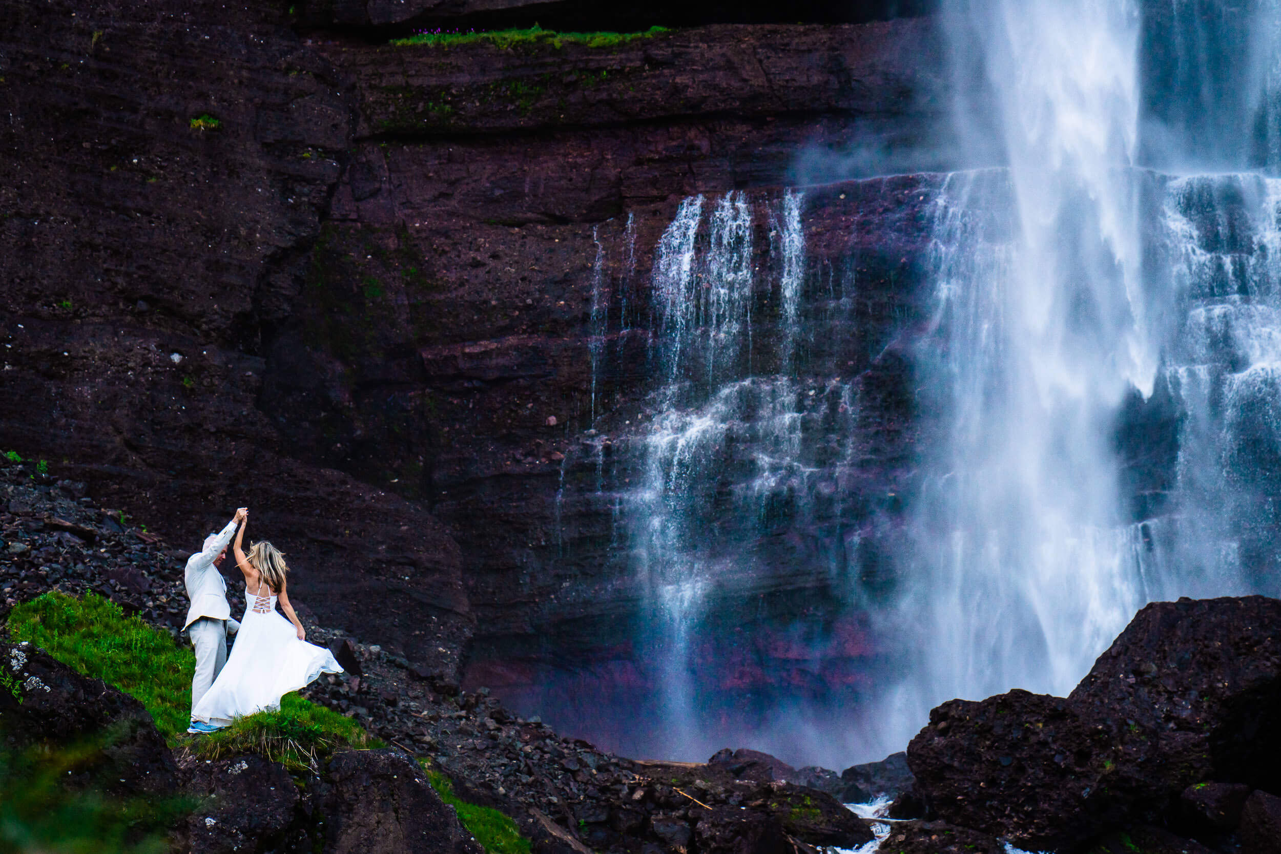 a bride and groom dancing on a rock below a waterfall 