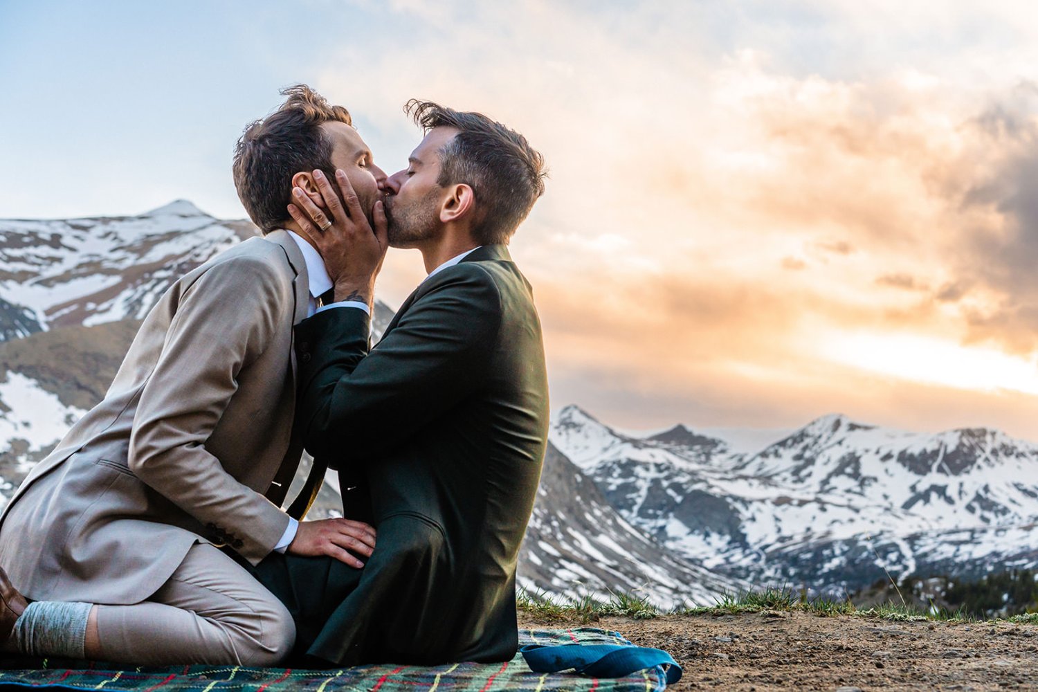Two men sharing an intimate moment on a blanket in front of a breathtaking mountain, captured beautifully in elopement photos.