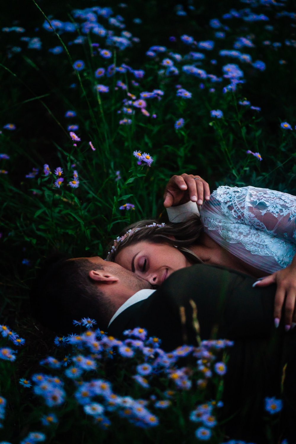 Capturing intimate elopement photos of a bride and groom peacefully lying in a field of flowers.