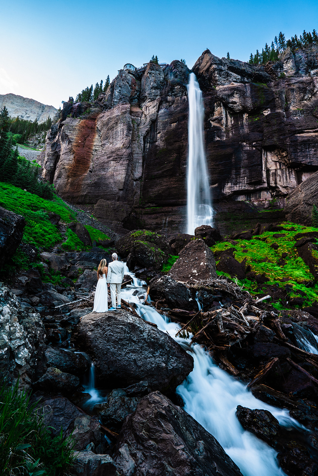 A bride and groom standing in front of a waterfall at one of the best places to elope in Colorado during their San Juan Mountains elopement in Telluride, Colorado.