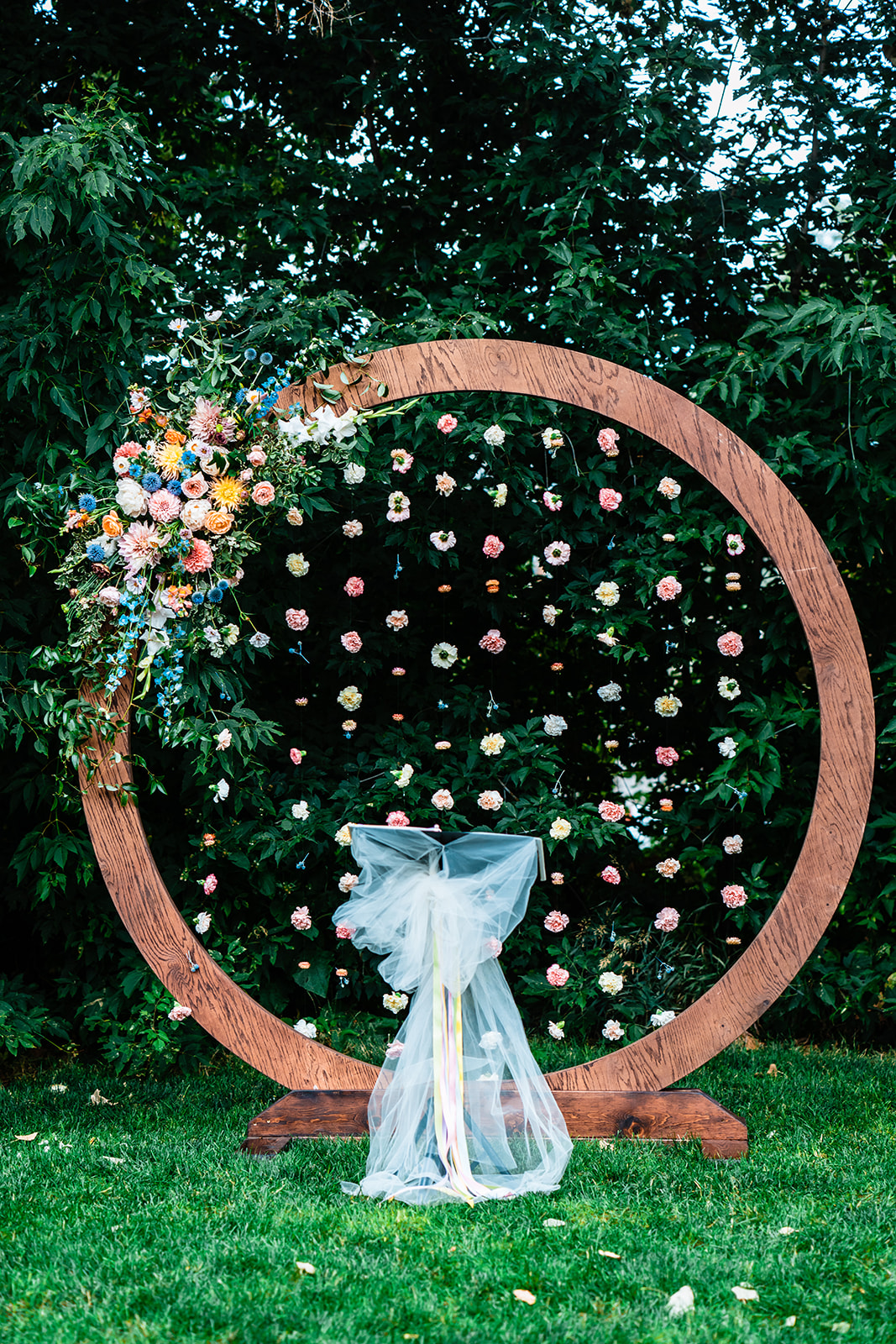 A wedding arch circle with real flowers decorate the wooden frame on a lush grassy lawn.