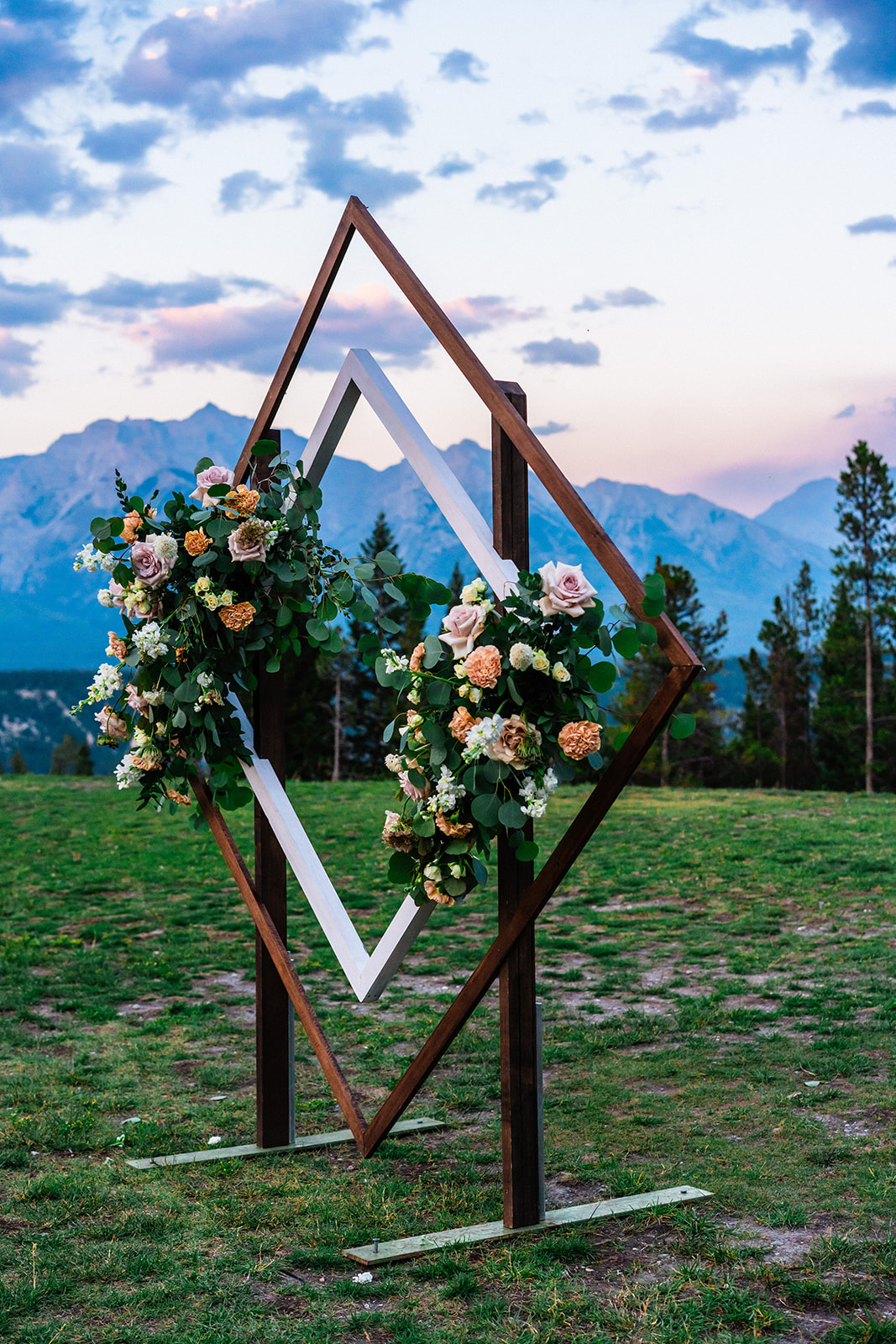 Diamond wedding arch with two bright and colorful floral decorations on either side set against a mountain sunset backdrop in Canmore, Canada during an intimate elopement.