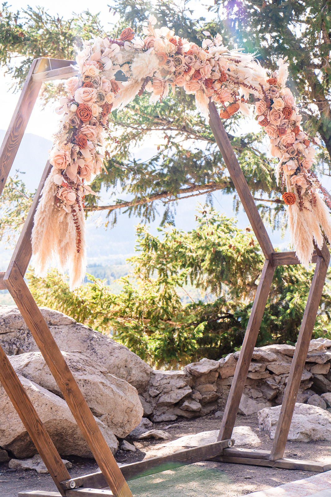 Wooden hexagon wedding arch pleasingly decorated with a plethora of boho styled florals set against a backdrop of mountains and trees during a Colorado intimate wedding at Sapphire Point in Breckenridge, Colorado. 