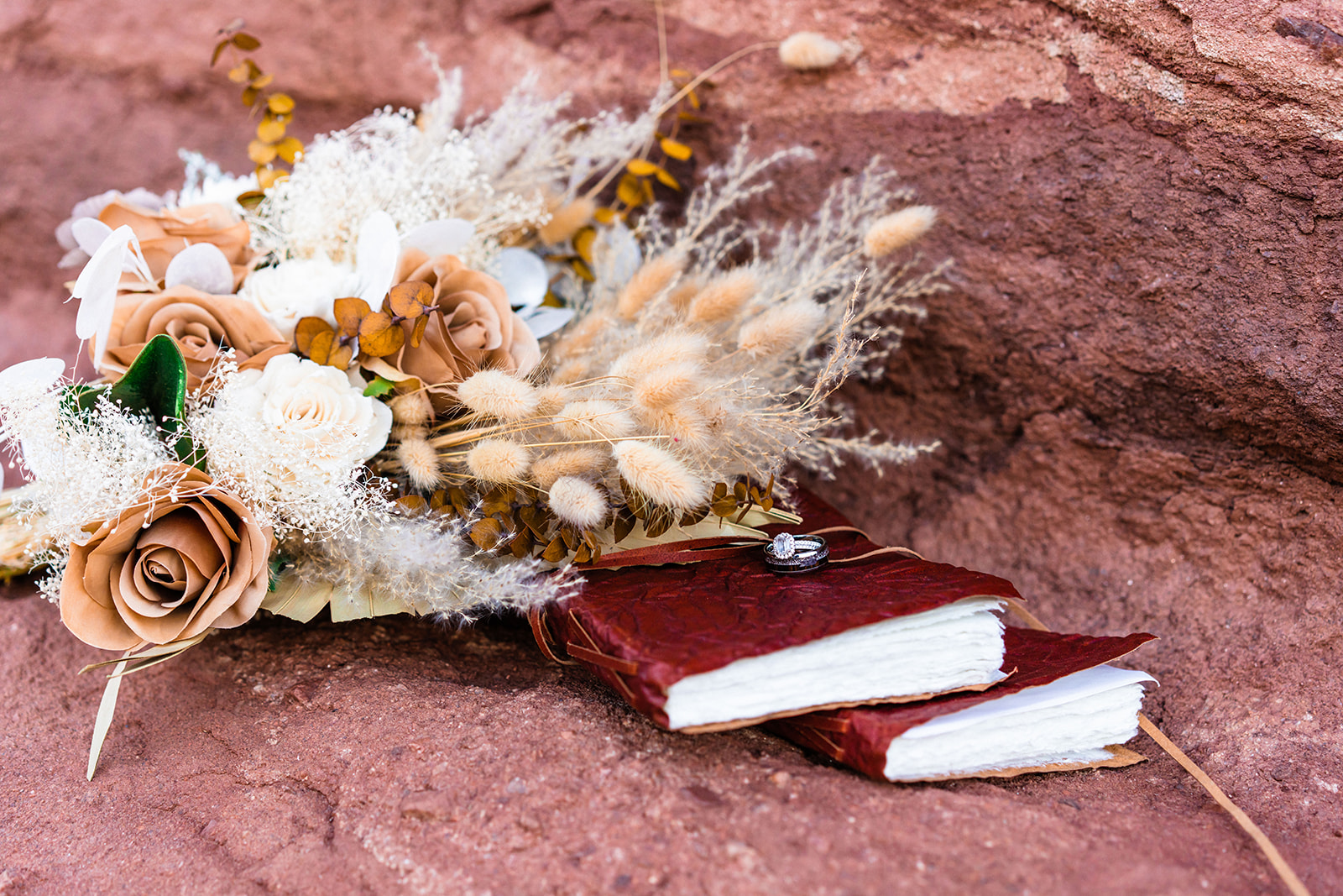 A bouquet for an elopement from a Colorado Springs florist sits upon a rock next to two vow books and wedding rings.