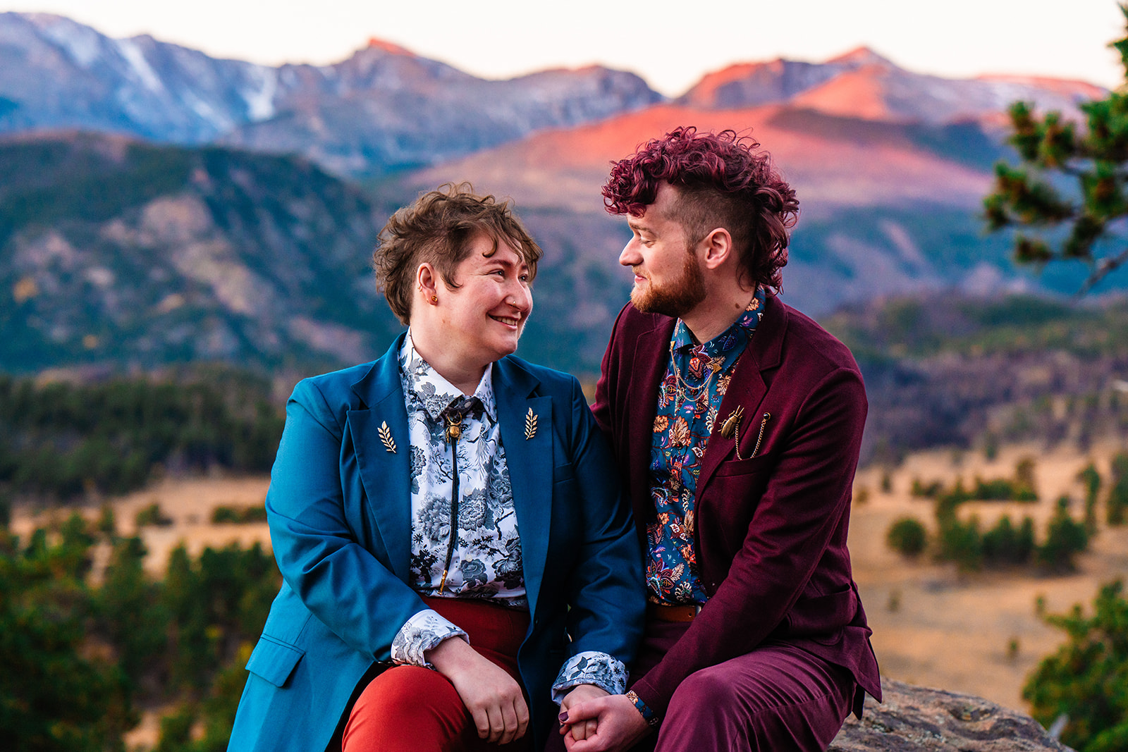 Two people wearing LGBTQ+ friendly elopement attire sitting on top of a mountain at sunrise during their Colorado elopement.