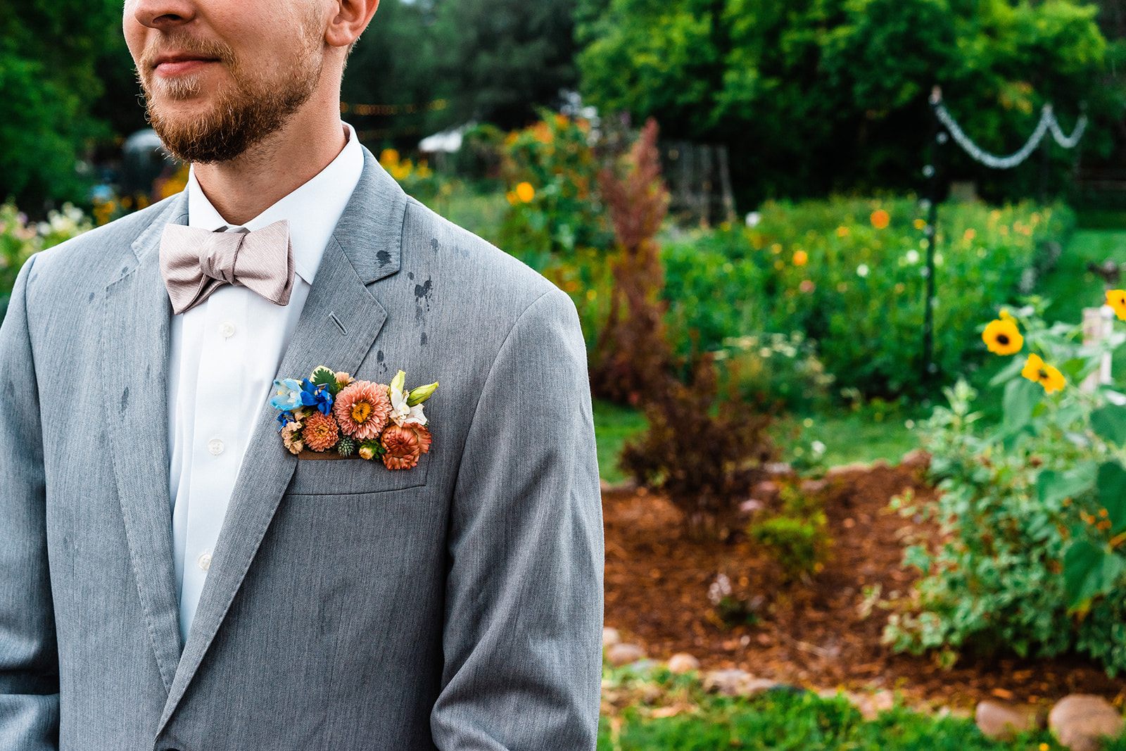 A groom in a gray suit standing in a garden.