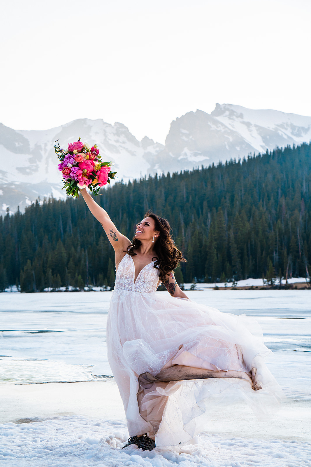 A bride in an elopement dress is holding flowers in the snow.