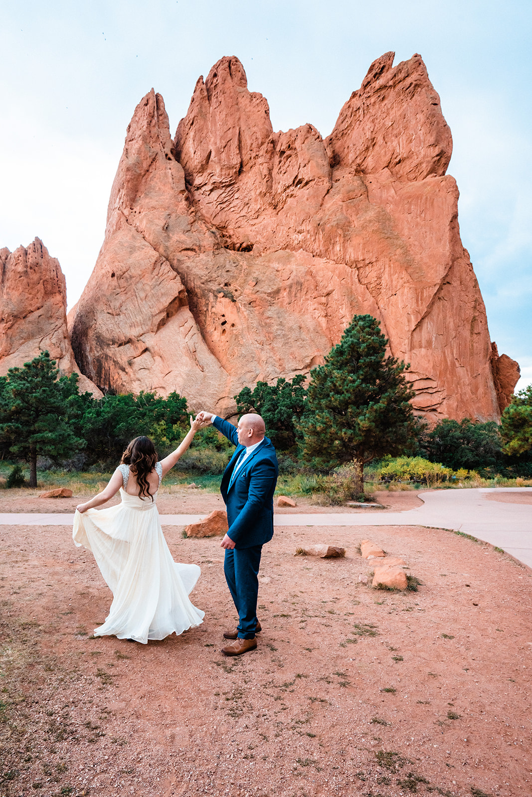 A bride twirling in her dress as the groom holds her hand along the Central Garden Trail during their Garden of the Gods elopement.