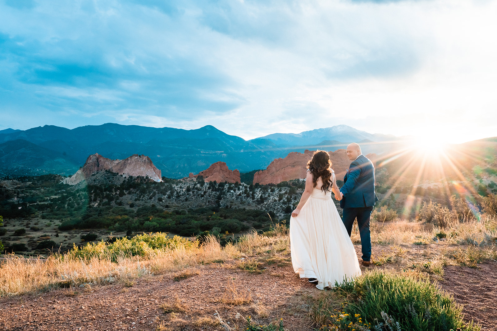 Newlyweds hold hands as the sun sets over the distant horizon as they enjoy the fleeting moments of their Garden of the Gods elopement at Mesa Overlook.