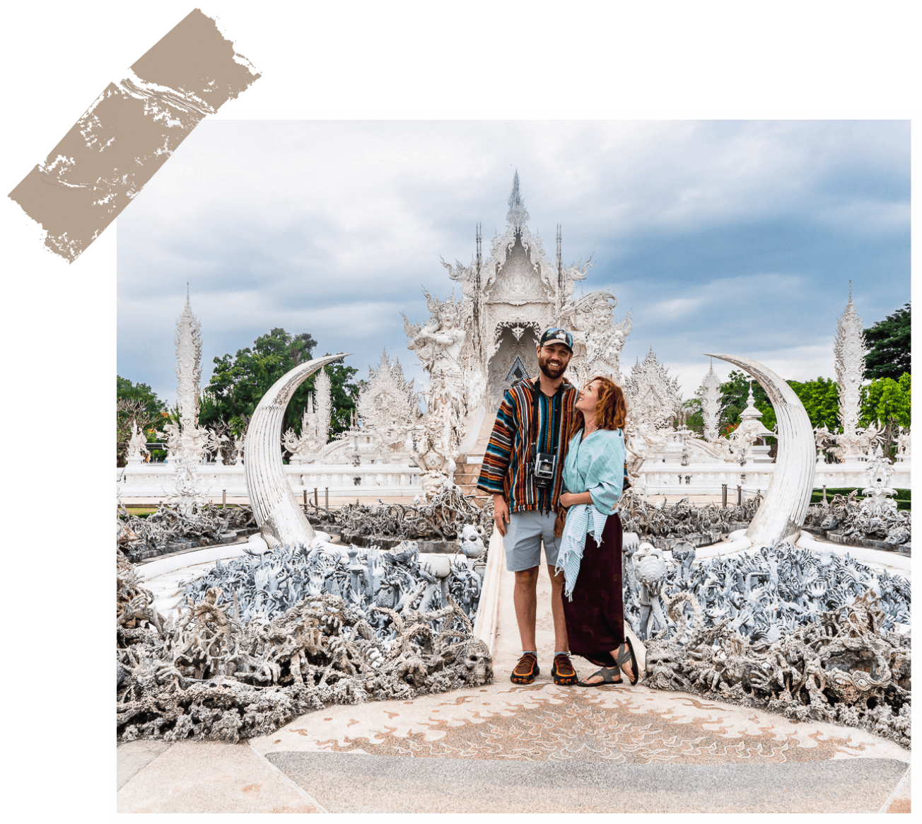 Meg and Kevin posing in front of the ornate white sculptures of the wat rong khun temple in thailand.